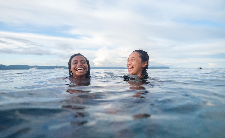 Two women treading water laugh at each other