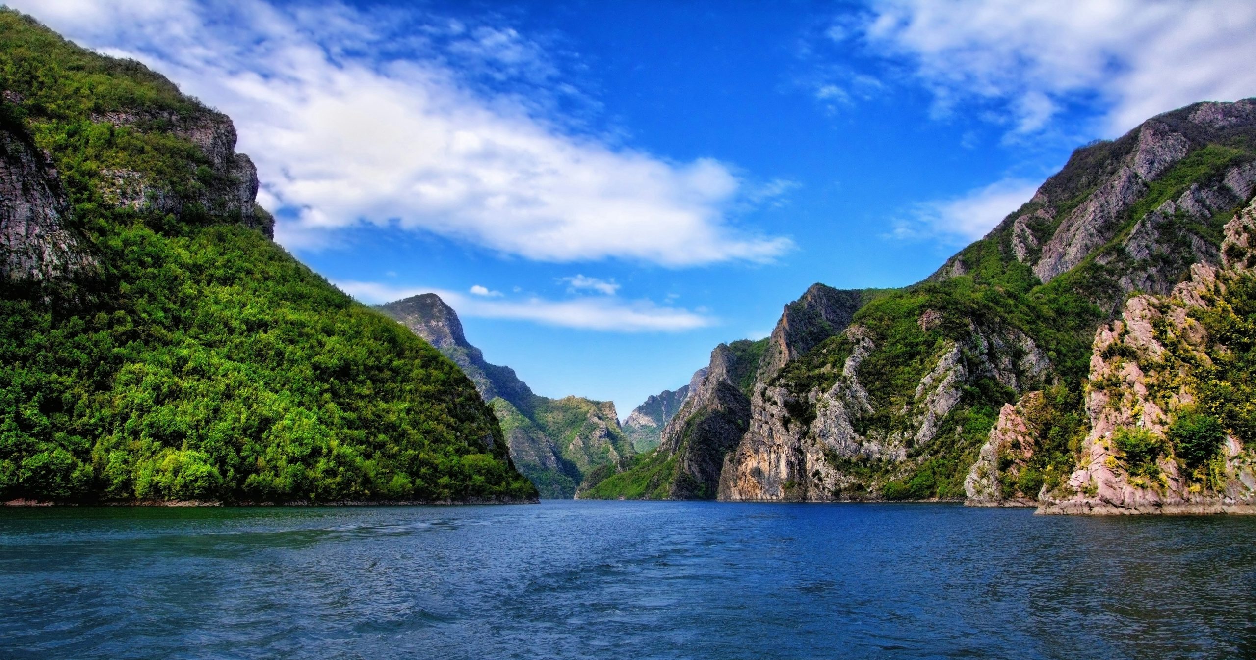 An image of an Albanian lake with steep mountainous sides and lush green vegetation