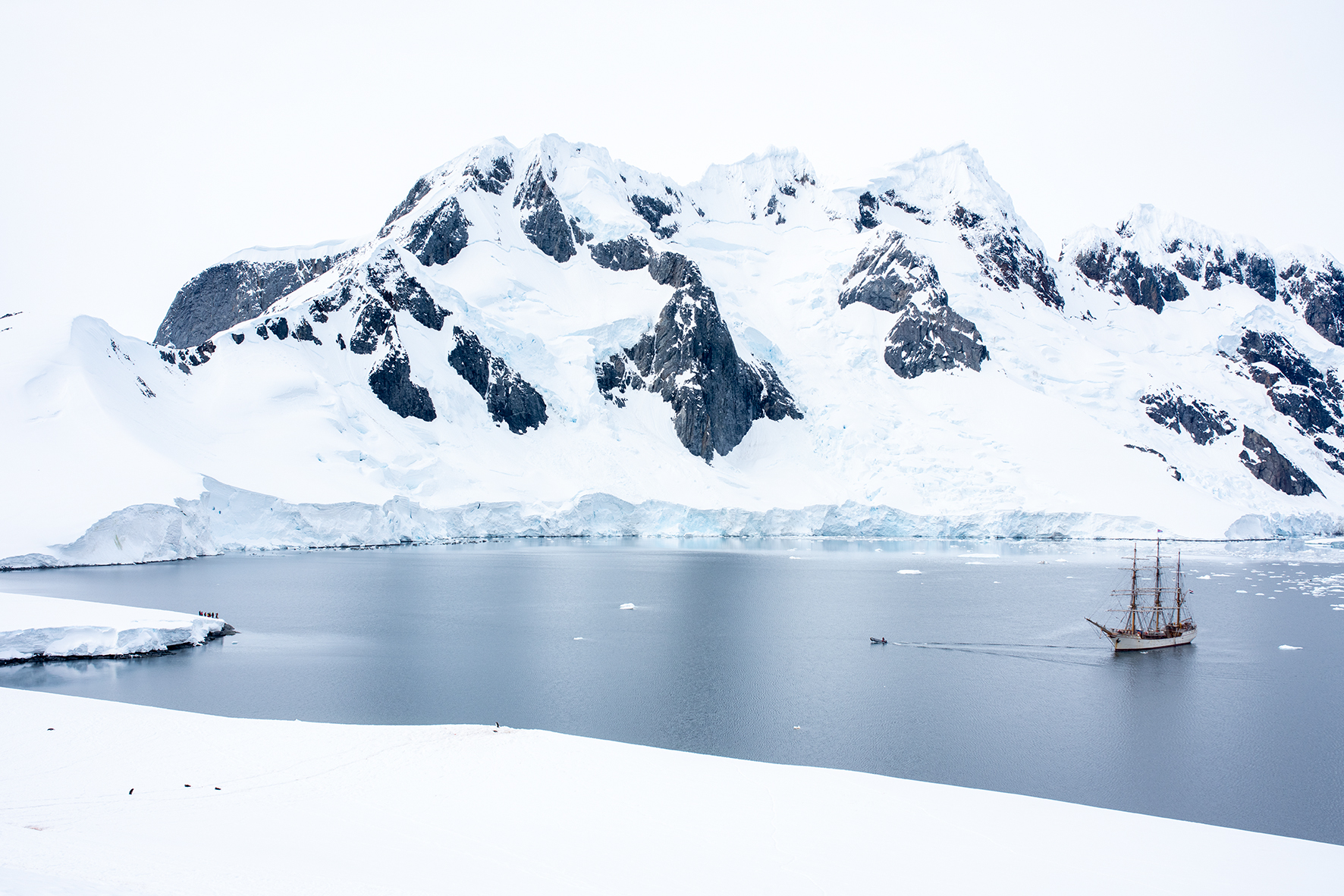 A Tall ship in Antarctica. The ship is dwarfed by the huge mountains and ice that surround it